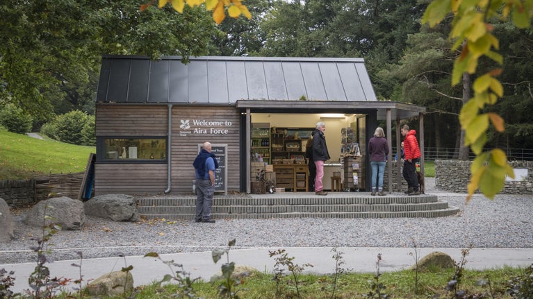 A visitor centre from the side with autumn trees beyond and people standing outside